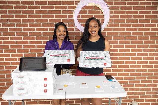 Two Famuan writers pose outside of SJGC building with Krispy Kreme donuts, hoping to en the student body .