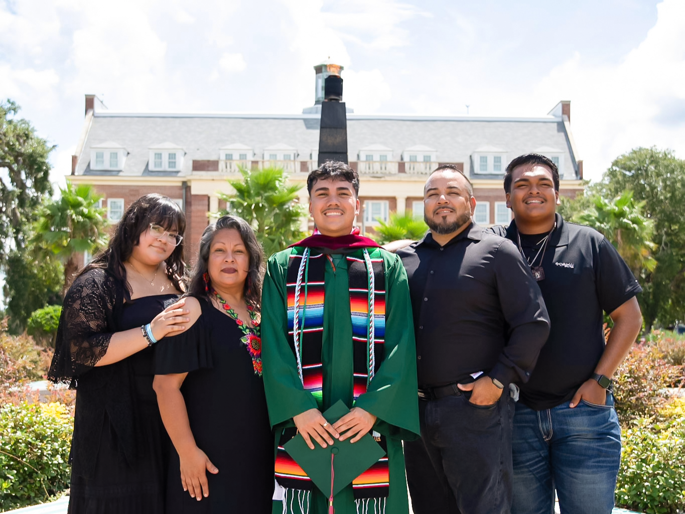 Luis Arriaga celebrates becoming the first in his family to obtain a four-year degree, surrounded by his parents and siblings. They are seen in front of the University's eternal flame, a moment symbolic of the motto, "Excellence With Caring."